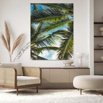 Looking up at lush green palm leaves against a bright blue sky, creating a tropical and relaxing coastal aesthetic.