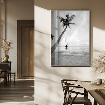 Monochrome photo of a woman swinging from a palm tree on a serene beach, ideal for minimalist or tropical coastal decor.