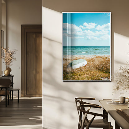 A small boat resting on a grassy shore with ocean waves and a bright blue sky, creating a peaceful coastal atmosphere.
