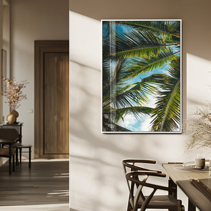 Looking up at lush green palm leaves against a bright blue sky, creating a tropical and relaxing coastal aesthetic.