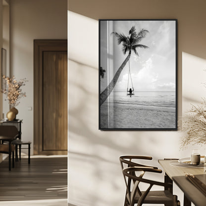Monochrome photo of a woman swinging from a palm tree on a serene beach, ideal for minimalist or tropical coastal decor.