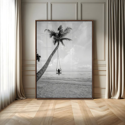 Monochrome photo of a woman swinging from a palm tree on a serene beach, ideal for minimalist or tropical coastal decor.