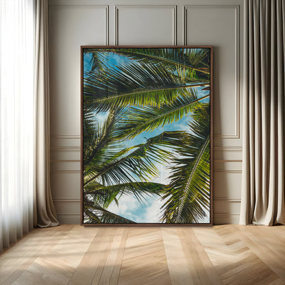 Looking up at lush green palm leaves against a bright blue sky, creating a tropical and relaxing coastal aesthetic.