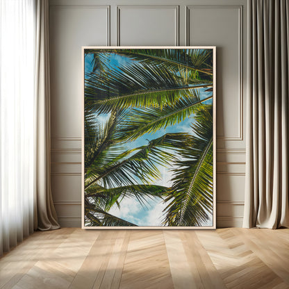 Looking up at lush green palm leaves against a bright blue sky, creating a tropical and relaxing coastal aesthetic.