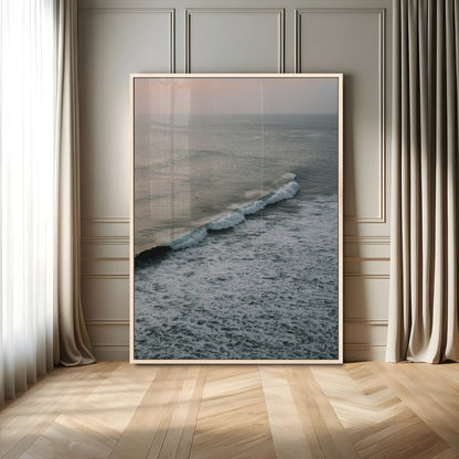 Aerial view of ocean waves rolling towards the shore under a soft sunset sky, creating a peaceful and minimalist coastal scene.