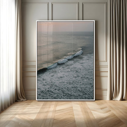 Aerial view of ocean waves rolling towards the shore under a soft sunset sky, creating a peaceful and minimalist coastal scene.