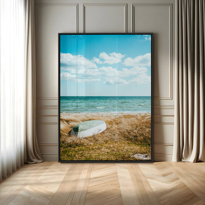 A small boat resting on a grassy shore with ocean waves and a bright blue sky, creating a peaceful coastal atmosphere.