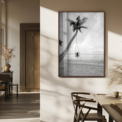 Monochrome photo of a woman swinging from a palm tree on a serene beach, ideal for minimalist or tropical coastal decor.