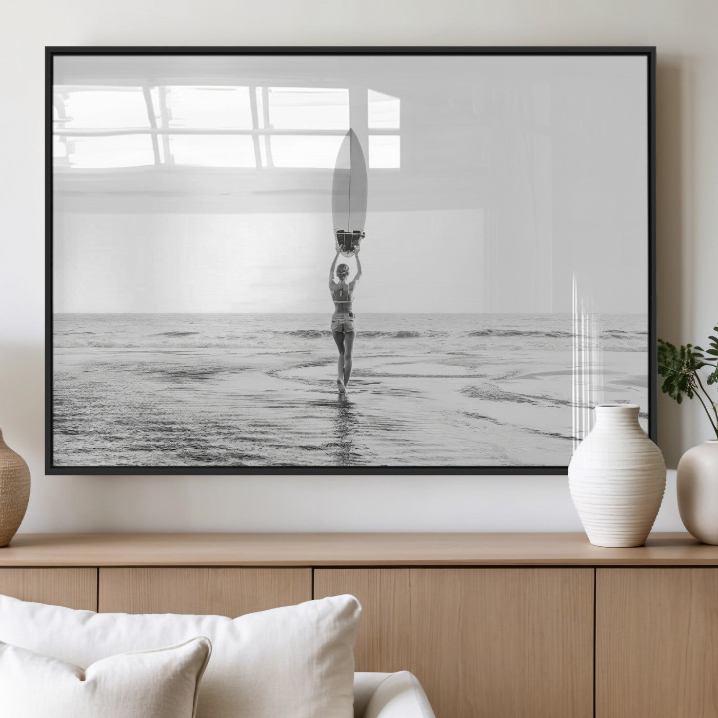 Black and white image of a female surfer holding a surfboard above her head while walking toward the ocean, creating a minimalist and bold coastal aesthetic.