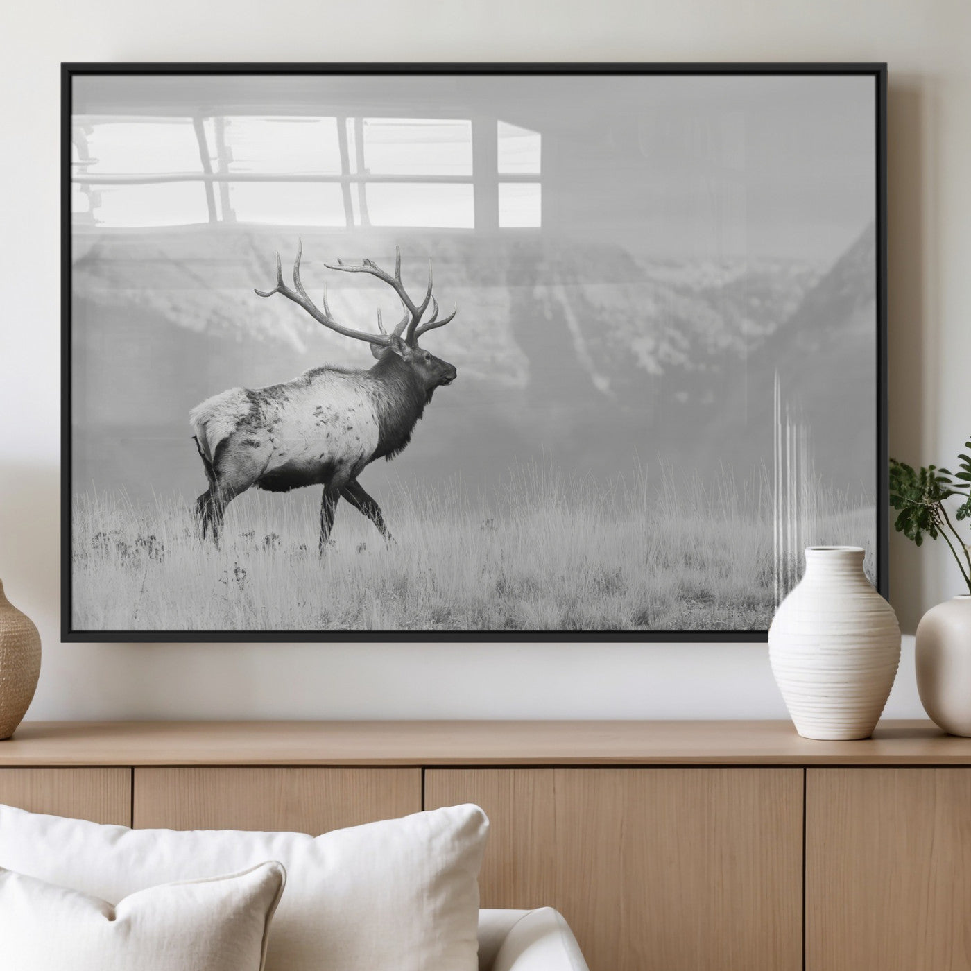 Black and white photograph of a majestic elk standing in a grassy field with snow-capped mountains in the background, creating a bold and rustic wilderness scene.