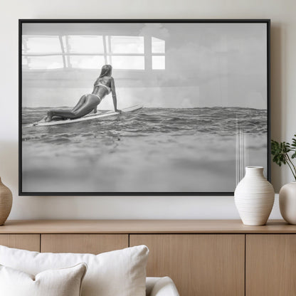 A black and white ocean scene featuring a surfer girl waiting on her board, gazing at the horizon, capturing a tranquil and adventurous coastal moment.