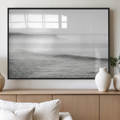 A black and white minimalist seascape featuring soft rolling waves and misty distant cliffs, creating a serene and timeless coastal atmosphere.