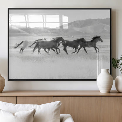 A black and white image of wild horses running freely across an open grassland, capturing the power and beauty of untamed nature in a rustic western setting.