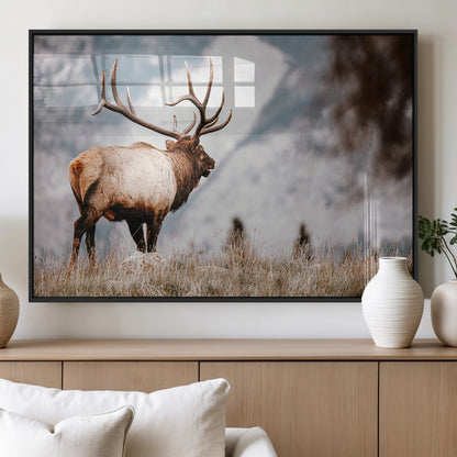 Majestic elk with large antlers standing in grass with snowy mountains in background, perfect for rustic cabin or lodge style decor.