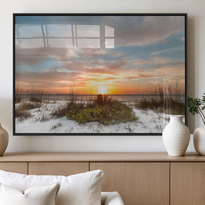A tranquil beach scene featuring golden sunset hues over the water, with grasses in the foreground and a peaceful, serene atmosphere.