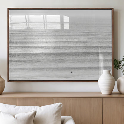 Monochrome photo of a lone surfer in calm layered waves, perfect for minimalist coastal or moody ocean-inspired wall decoration.