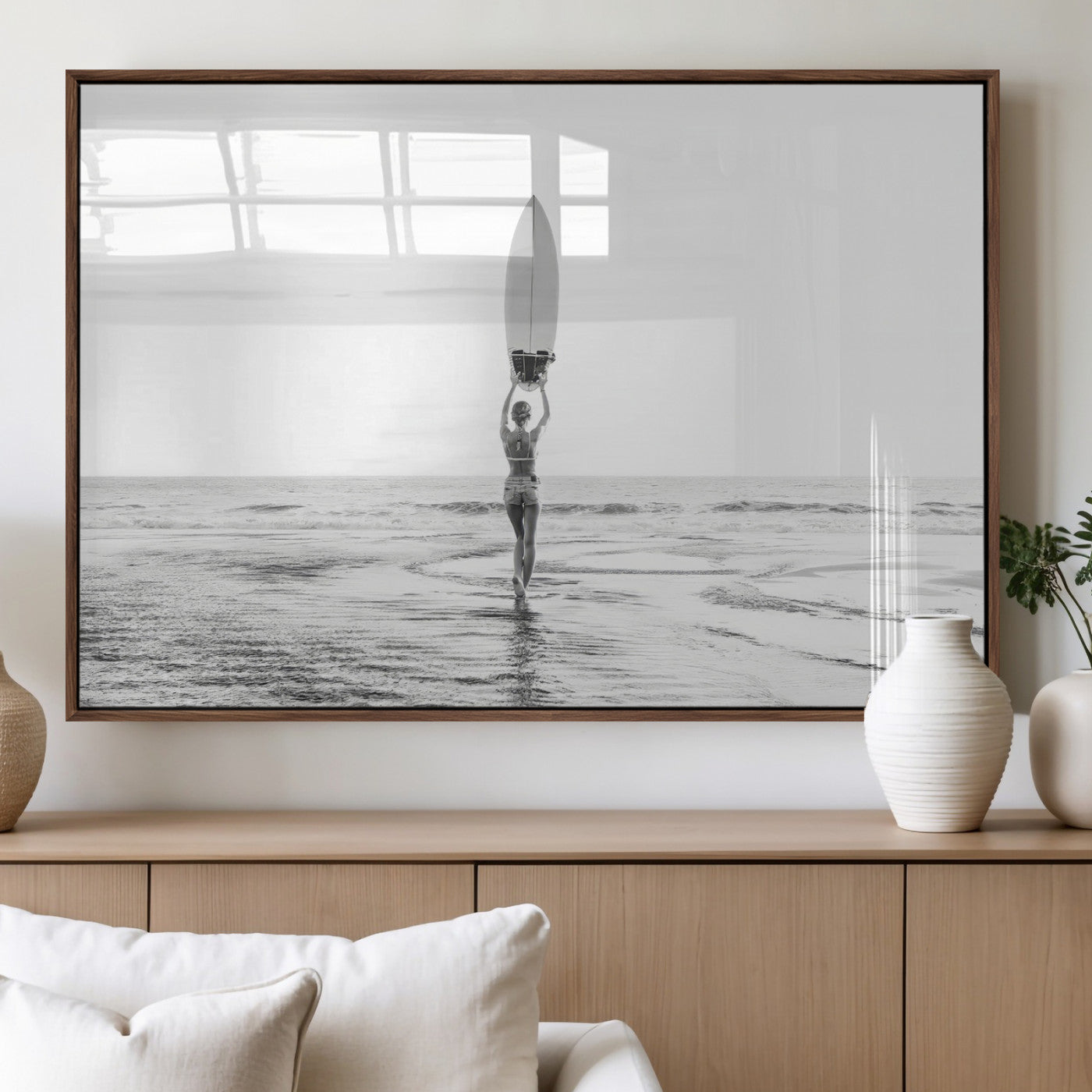Black and white image of a female surfer holding a surfboard above her head while walking toward the ocean, creating a minimalist and bold coastal aesthetic.