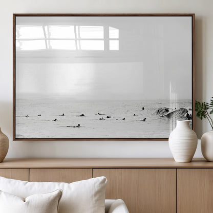 A group of surfers floating in the ocean, waiting for waves under a vast, moody sky, captured in black and white.