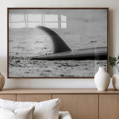 A black and white close-up of a surfboard fin resting on the sandy shore, highlighting minimalist beach aesthetics and classic surf culture.
