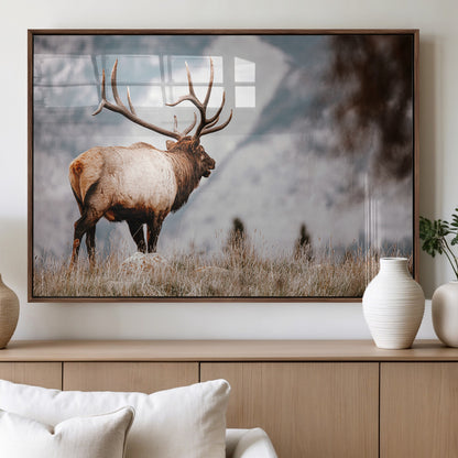 Majestic elk with large antlers standing in grass with snowy mountains in background, perfect for rustic cabin or lodge style decor.