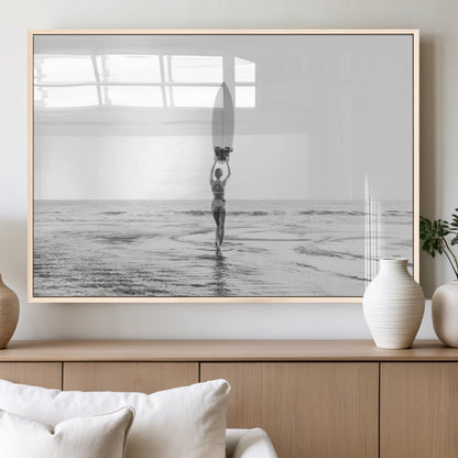 Black and white image of a female surfer holding a surfboard above her head while walking toward the ocean, creating a minimalist and bold coastal aesthetic.