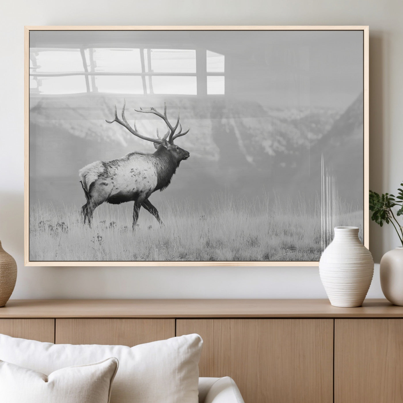 Black and white photograph of a majestic elk standing in a grassy field with snow-capped mountains in the background, creating a bold and rustic wilderness scene.