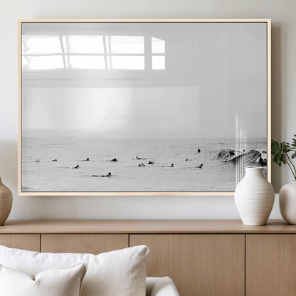 A group of surfers floating in the ocean, waiting for waves under a vast, moody sky, captured in black and white.