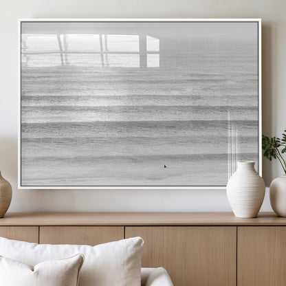 Monochrome photo of a lone surfer in calm layered waves, perfect for minimalist coastal or moody ocean-inspired wall decoration.