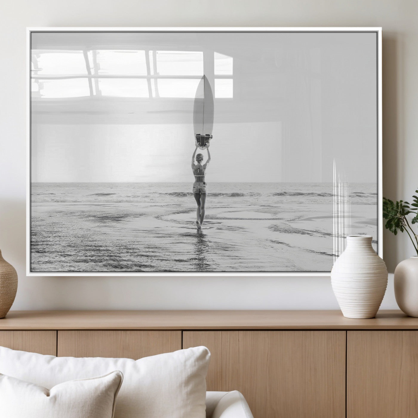 Black and white image of a female surfer holding a surfboard above her head while walking toward the ocean, creating a minimalist and bold coastal aesthetic.