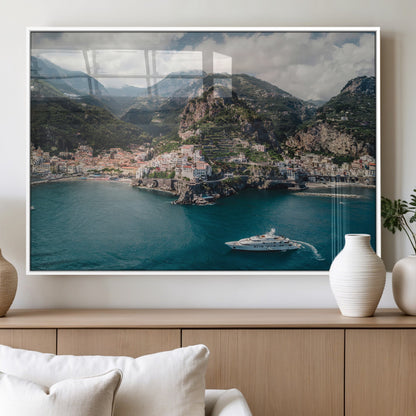 Aerial view of Amalfi Coast, Italy, with colorful hillside houses, lush green mountains, and a luxury yacht sailing in turquoise waters.