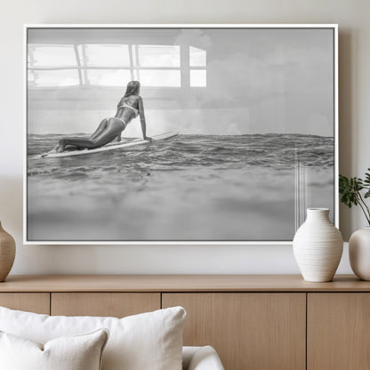 A black and white ocean scene featuring a surfer girl waiting on her board, gazing at the horizon, capturing a tranquil and adventurous coastal moment.