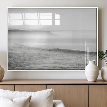 A black and white minimalist seascape featuring soft rolling waves and misty distant cliffs, creating a serene and timeless coastal atmosphere.