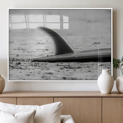 A black and white close-up of a surfboard fin resting on the sandy shore, highlighting minimalist beach aesthetics and classic surf culture.