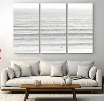 Monochrome photo of a lone surfer in calm layered waves, perfect for minimalist coastal or moody ocean-inspired wall decoration.