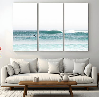 Minimalist photo of a lone surfer on calm aqua waves under bright sky, perfect for Scandinavian coastal or serene ocean-inspired home decor.