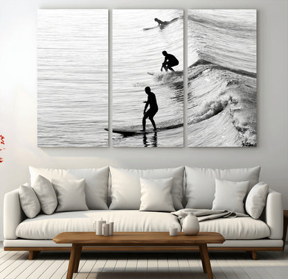 Black and white photo of surfers riding waves in a moody, high-contrast scene, ideal for modern coastal or surf-inspired home decor.