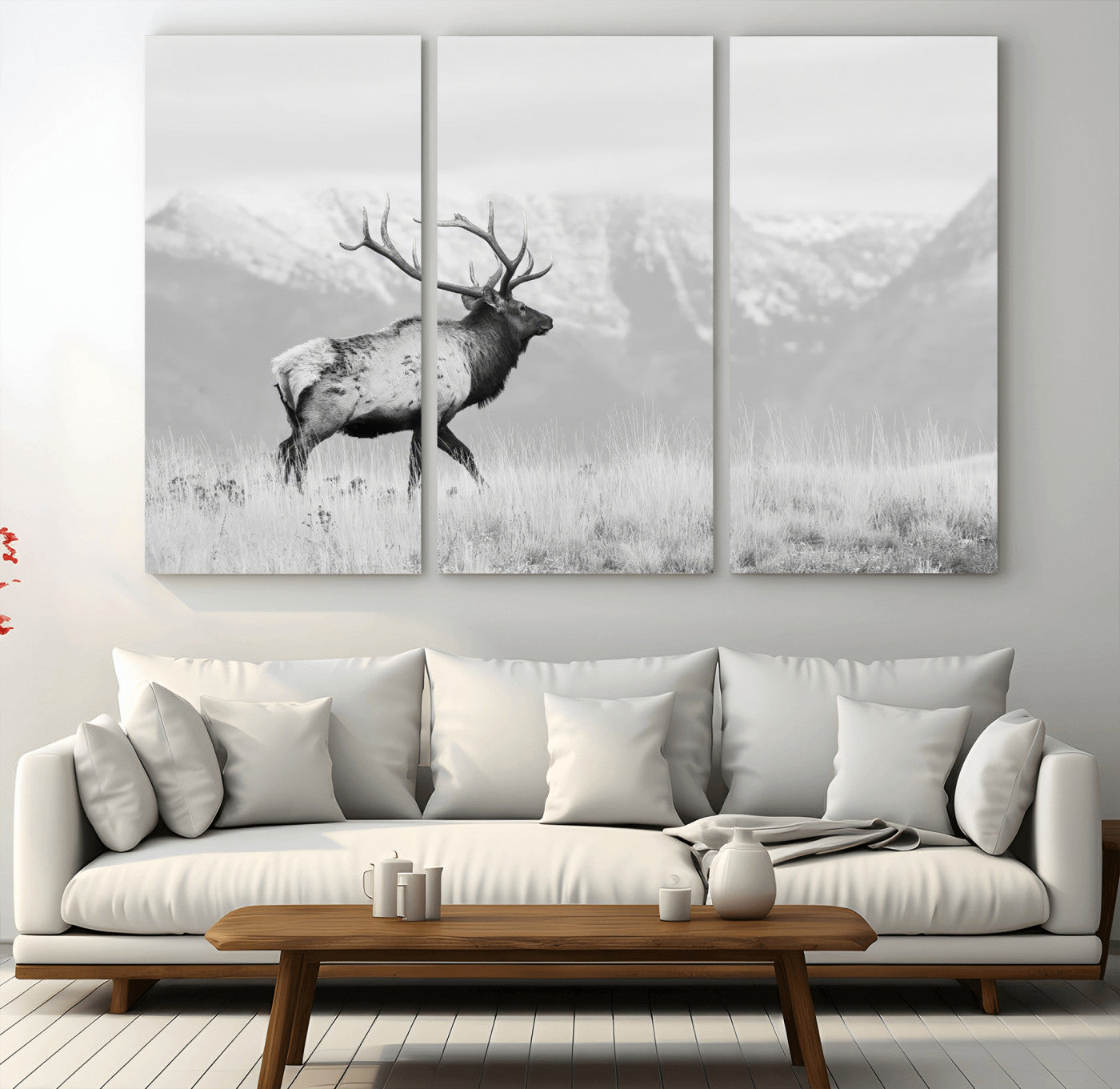 Black and white photograph of a majestic elk standing in a grassy field with snow-capped mountains in the background, creating a bold and rustic wilderness scene.
