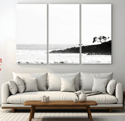 Black and white photo of a surfer standing on rocky cliffs, gazing at the waves, embodying the spirit of adventure and solitude.