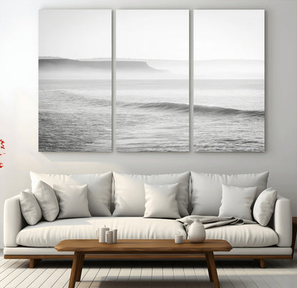A black and white minimalist seascape featuring soft rolling waves and misty distant cliffs, creating a serene and timeless coastal atmosphere.