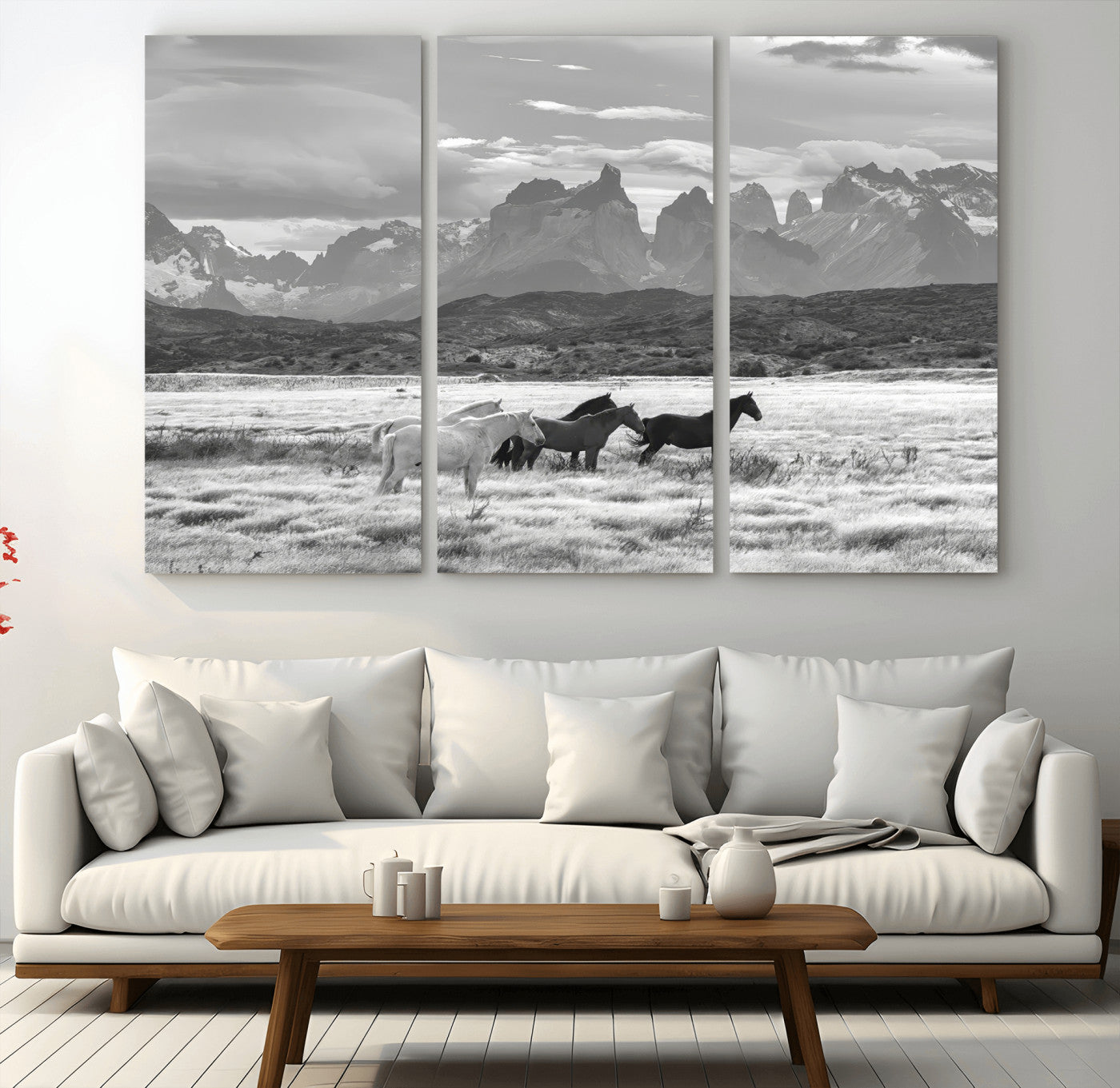 A black and white landscape of wild horses grazing in a vast grassland with towering mountains in the background, creating a moody and rustic western aesthetic.