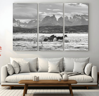 A black and white landscape of wild horses grazing in a vast grassland with towering mountains in the background, creating a moody and rustic western aesthetic.