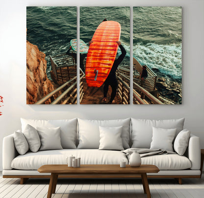 A surfer carrying a bold orange surfboard down a rugged staircase toward the ocean, bathed in golden hour light, capturing the energy of coastal adventure.