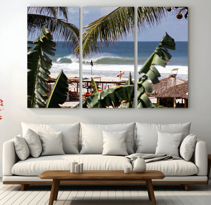 Canvas wall art of a tropical surf scene framed by palm trees, with a surfer on the shore and waves rolling in, ideal for beach-themed decor.