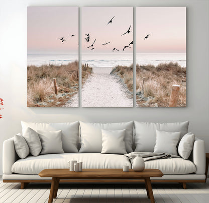 A peaceful coastal pathway leading to the ocean, with birds flying across a soft pastel sky, creating a calm and scenic beach atmosphere.