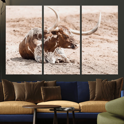 Texas Longhorn bull resting on dusty ground with warm tones, ideal for rustic western or farmhouse-themed wall decor.