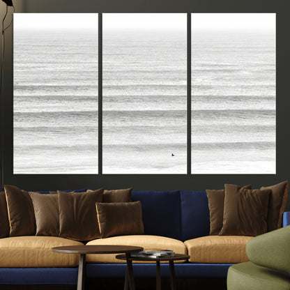 Monochrome photo of a lone surfer in calm layered waves, perfect for minimalist coastal or moody ocean-inspired wall decoration.