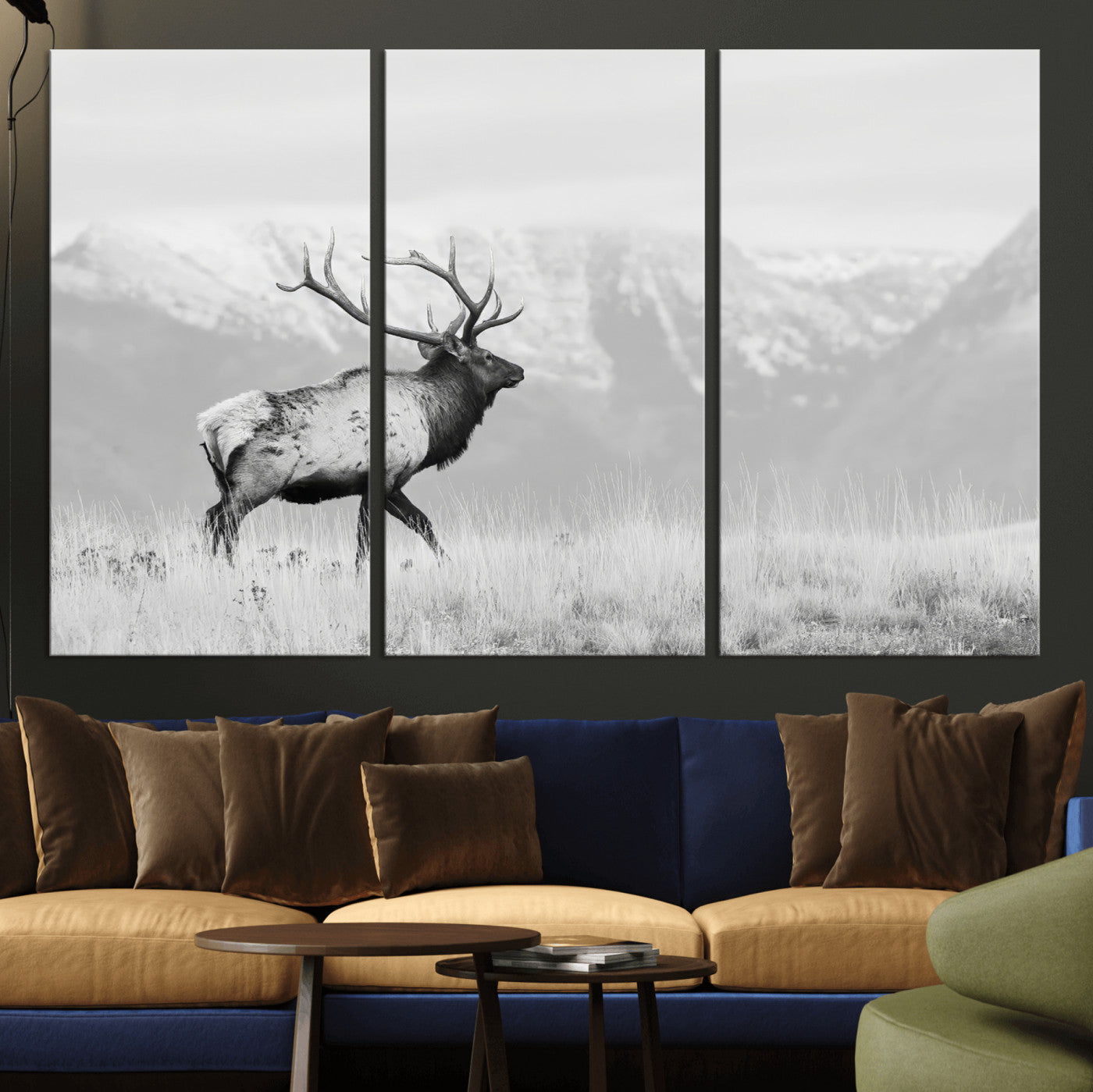 Black and white photograph of a majestic elk standing in a grassy field with snow-capped mountains in the background, creating a bold and rustic wilderness scene.