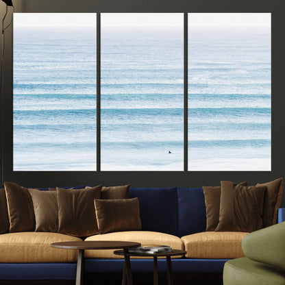 Minimalist ocean view with soft blue waves and a lone surfer, creating a serene and airy coastal aesthetic, perfect for tranquil home decor.