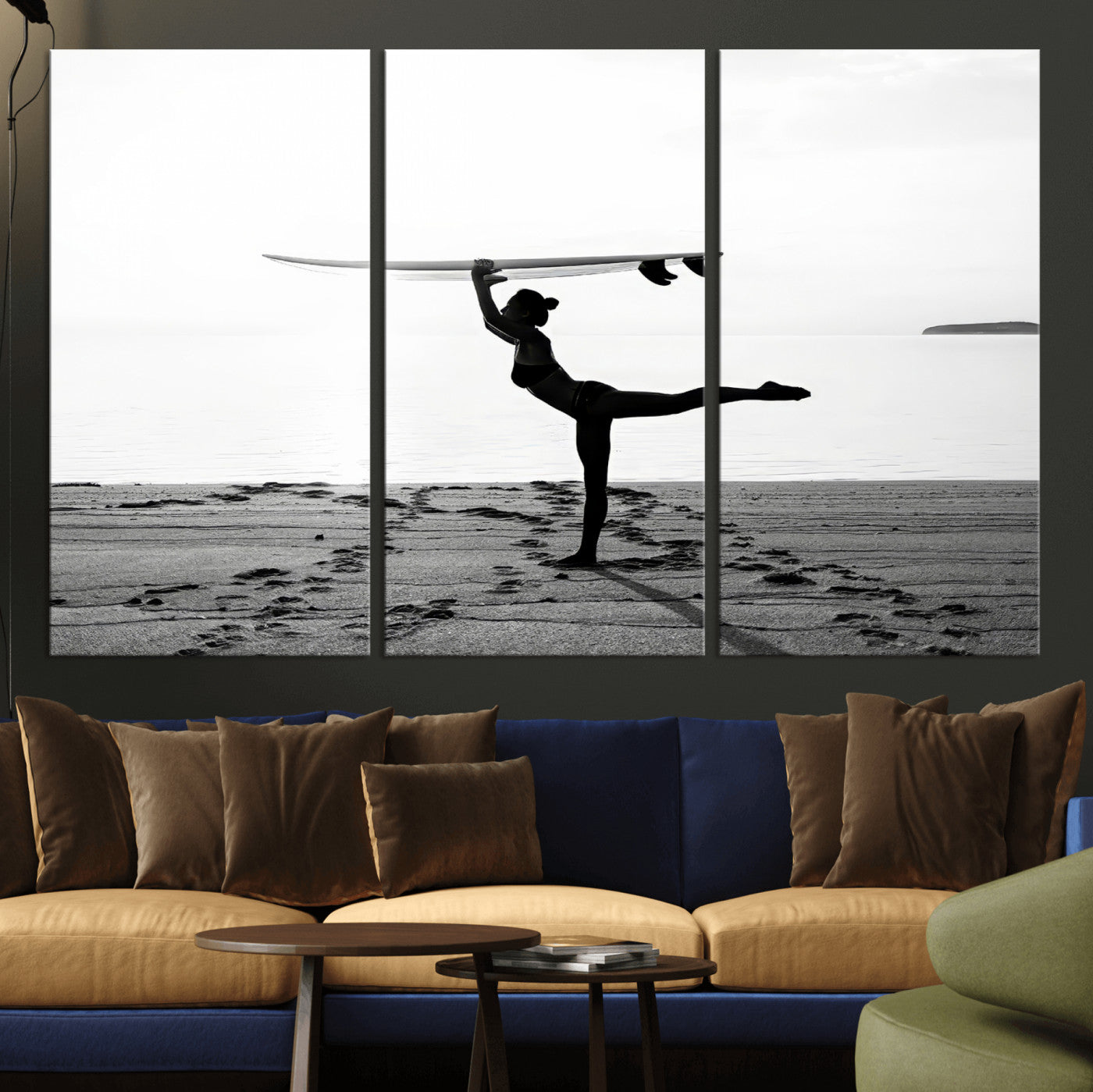 A woman balances a surfboard on her head while striking a yoga pose on the beach, silhouetted against a calm ocean horizon.
