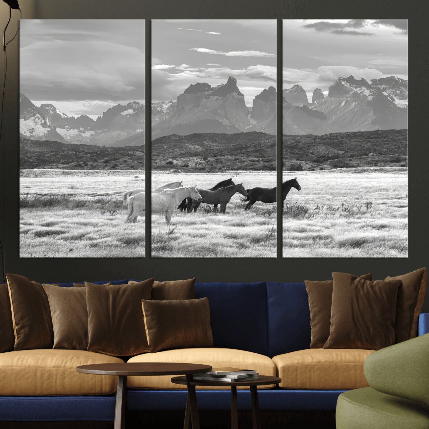 A black and white landscape of wild horses grazing in a vast grassland with towering mountains in the background, creating a moody and rustic western aesthetic.